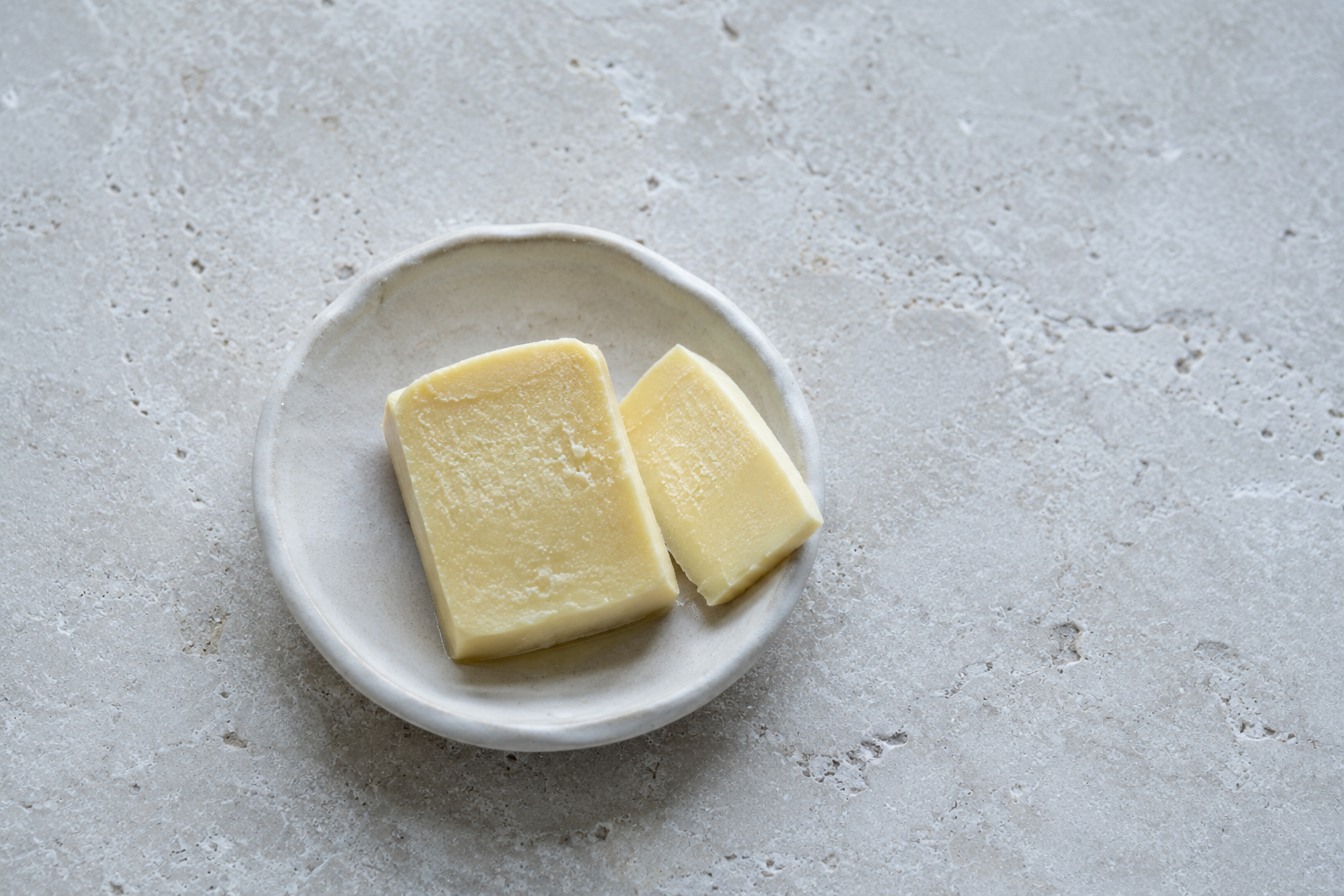 Two slabs of pale cultured butter on a small ceramic dish on a limestone bench