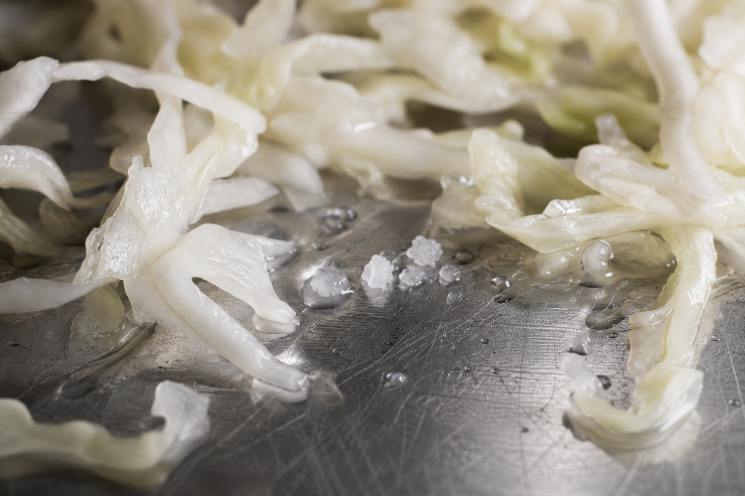 Salt drawing water out of shredded cabbage on a stainless steel bench