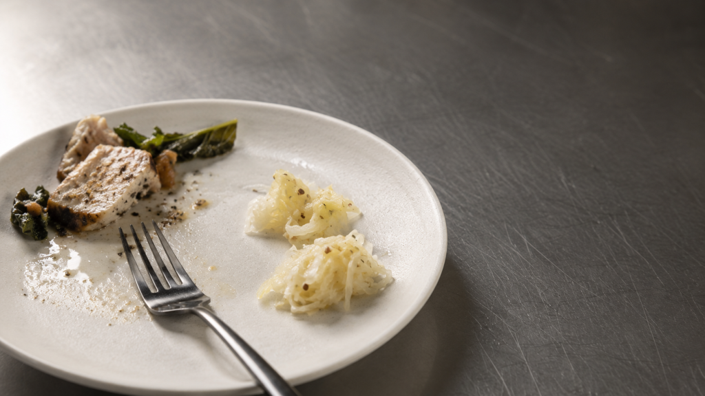 A simple plated meal mostly eaten, with two forkfuls of fermented cabbage and caraway beside it on a dark steel bench