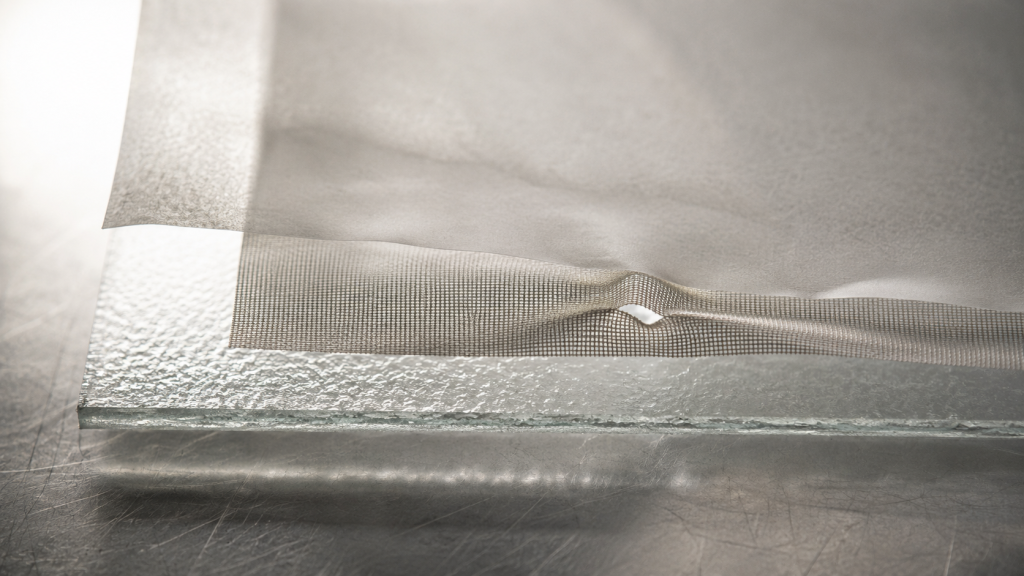 Layered translucent sheets of glass, fine mesh and film held to the light, the boundary distorted and let through at one small point.