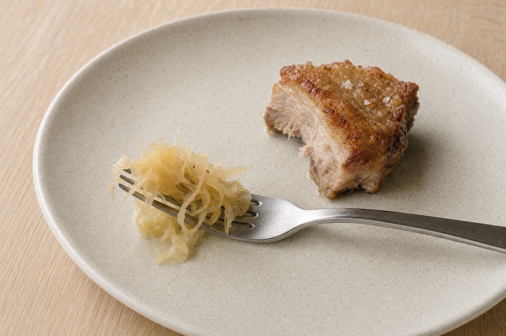 A fork resting on a plate with a small tangle of sauerkraut on its tines, beside roast pork