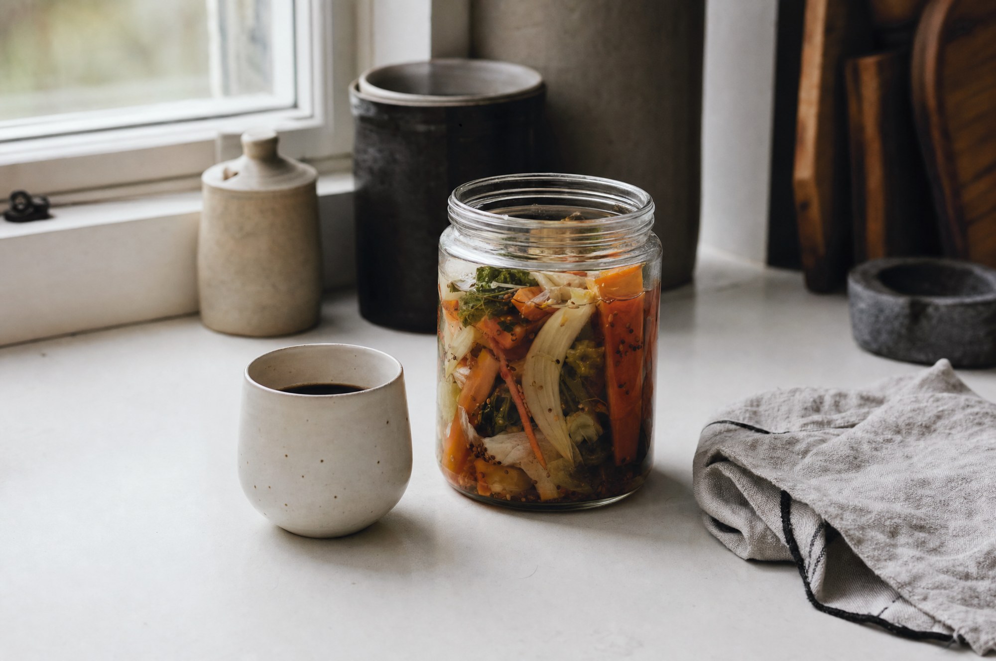 Black coffee and a jar of fermented vegetables on a kitchen bench in morning light