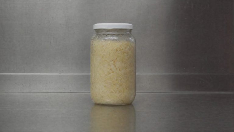 Sealed supermarket jar of pale sauerkraut on a bare steel shelf