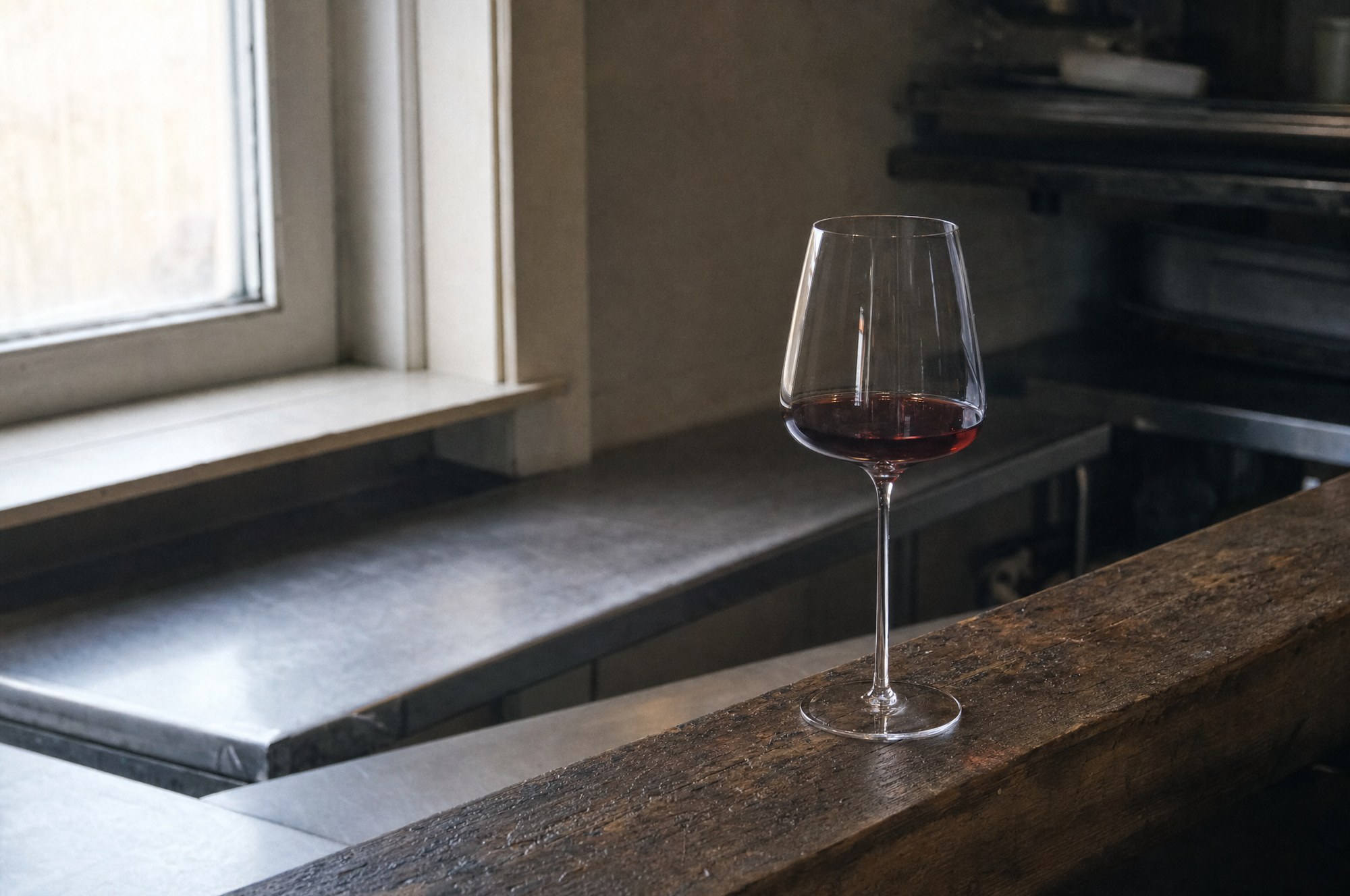 Glass of red wine on a timber kitchen pass in window light