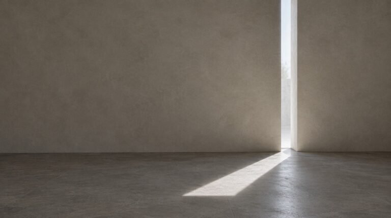 A slot of window light crossing a bare plaster wall and marking the concrete floor